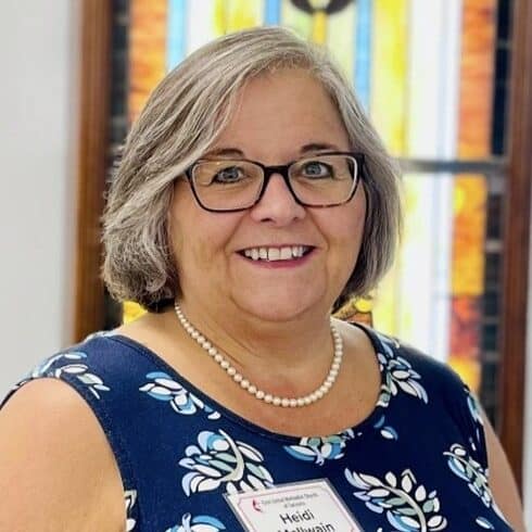 Heidi Mcilwain, staff member at First United Methodist Church of Sarasota, smiling in front of stained glass
