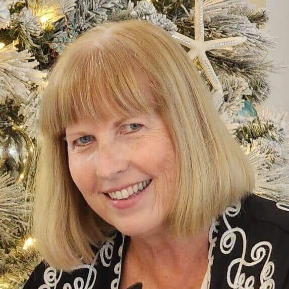 A staff member at First United Methodist Church of Sarasota smiling in front of a decorated Christmas tree.
