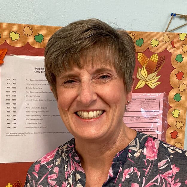 A staff member at First United Methodist Church of Sarasota smiles in front of a classroom bulletin board.