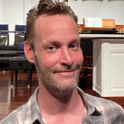 Portrait of a man smiling in the sanctuary of First United Methodist Church of Sarasota, with organ and piano visible in the background.