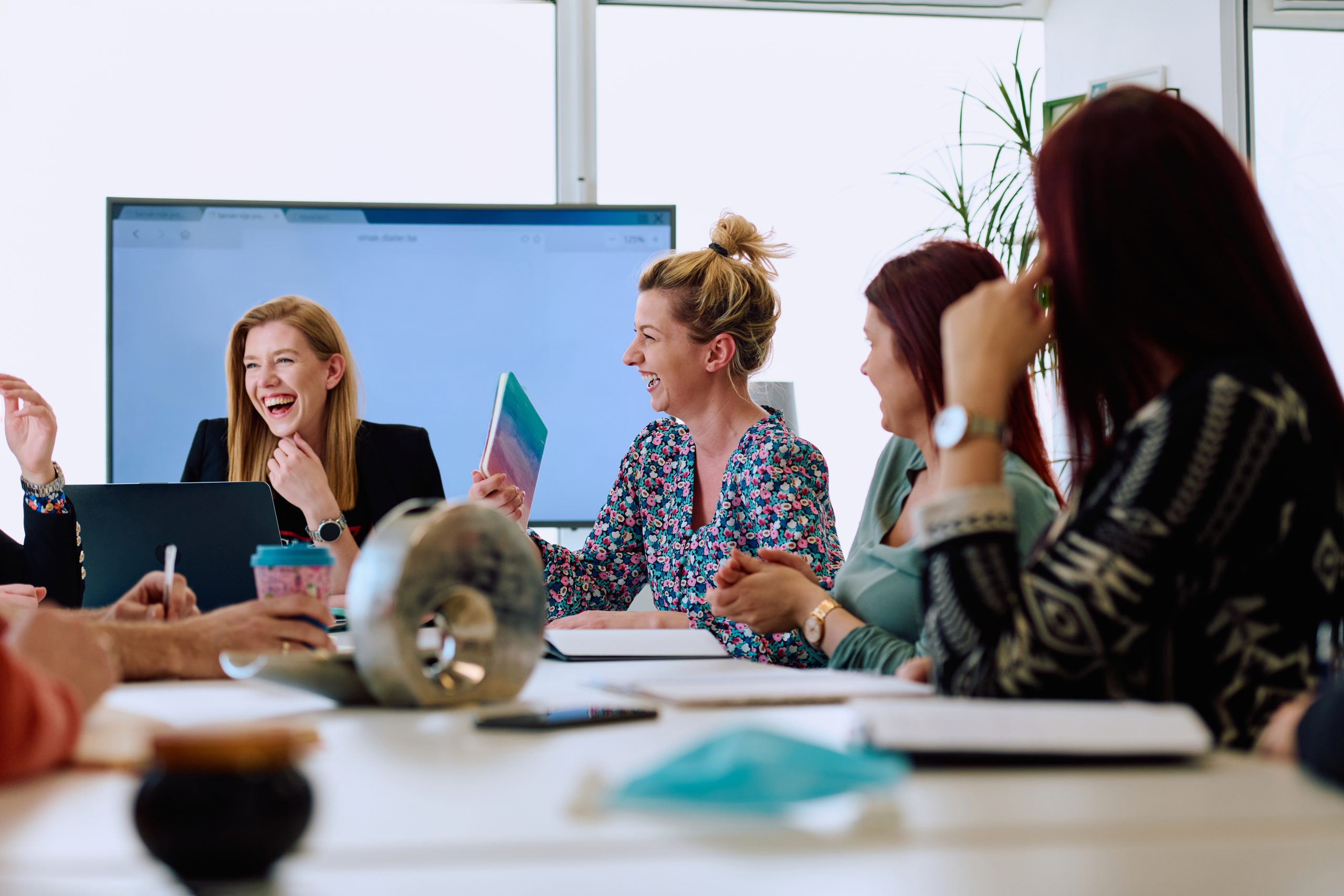 A diverse team of business professionals engaged in a discussion about projects in a modern glass walled office.